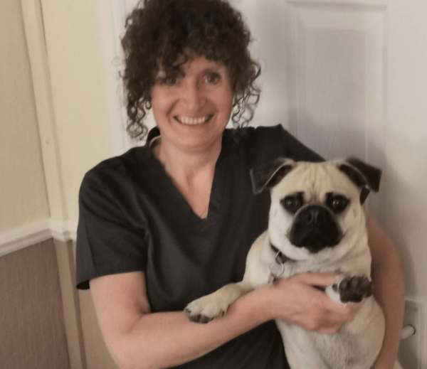 Image shows Receptionist at Chorley vets smiling holding a Pug