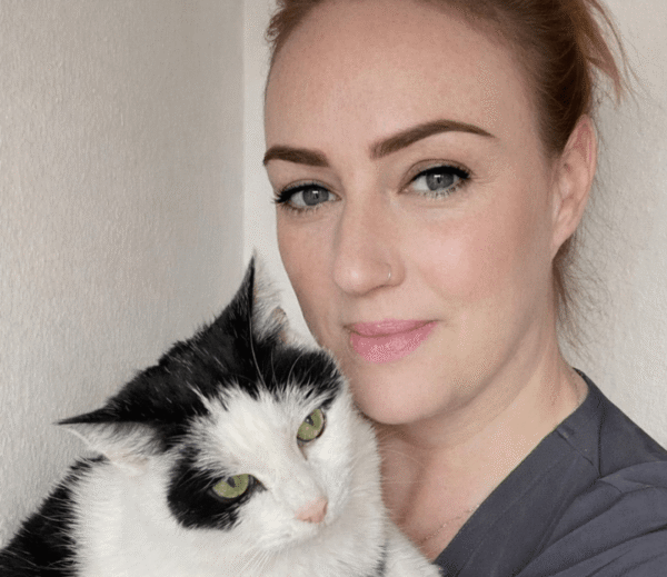 Sam Nelson, receptionist at Chorley Vets, holding a black and white cat while looking at the camera.